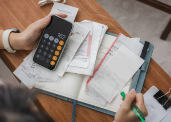 Close up a woman managing her home finances with a smartphone, she reviews financial bills. Concepts include financial planning, taxes, spending, budgeting, and financial challenges.