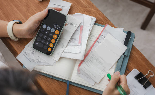 Close up a woman managing her home finances with a smartphone, she reviews financial bills. Concepts include financial planning, taxes, spending, budgeting, and financial challenges.