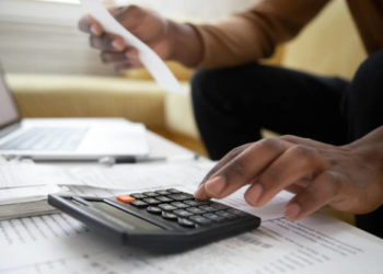 Close up of african american man with calculator checking bills at home. Savings, finances, economy concept. Black small business owner calculating income and planning budget