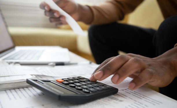 Close up of african american man with calculator checking bills at home. Savings, finances, economy concept. Black small business owner calculating income and planning budget