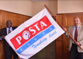 Mr Eric Kipkemei Bett (left) a board member at the Postal Corporation of Kenya hands over the corporation’s flag to Mr Peter Kanaiya, the new board chairman.