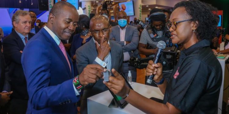 Safaricom M-Pesa Segment Marketing, Sheila Chenye (Right), demonstrates how a braille smart watch works to Cabinet Secretary, Ministry of ICT, Innovation & Youth Affairs, Hon. Joseph Mucheru (Left) and Chief Executive Officer, Safaricom PLC, Peter Ndegwa (Center) during the FinTech Innovation Week event at the Michael Joseph Center in Nairobi.