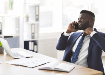 Stressed young african american manager talking by phone with colleagues in office, holding tie, copy space