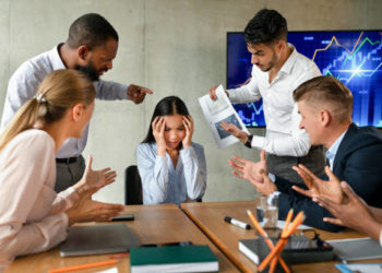 Conflicts At Work. Unhappy Asian Female Employee Suffering From Mobbing And Bullying In Office, Upset Employee Lady Covering Ears While Aggressive Coworkers Shouting At Her During Corporate Meeting