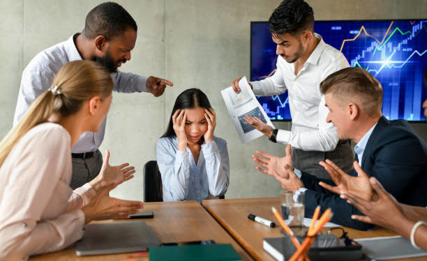 Conflicts At Work. Unhappy Asian Female Employee Suffering From Mobbing And Bullying In Office, Upset Employee Lady Covering Ears While Aggressive Coworkers Shouting At Her During Corporate Meeting