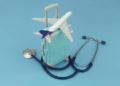 Airplane on travel suitcase and stethoscope on blue background. Travel insurance and medical tourism concept.