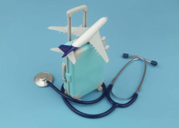 Airplane on travel suitcase and stethoscope on blue background. Travel insurance and medical tourism concept.