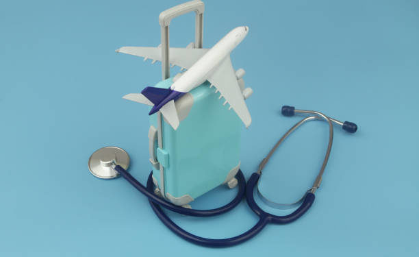 Airplane on travel suitcase and stethoscope on blue background. Travel insurance and medical tourism concept.